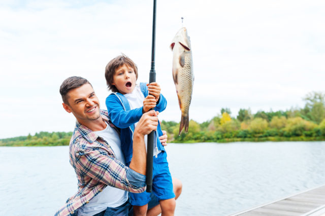 It is so big! Father and son stretching a fishing rod with fish on the hook